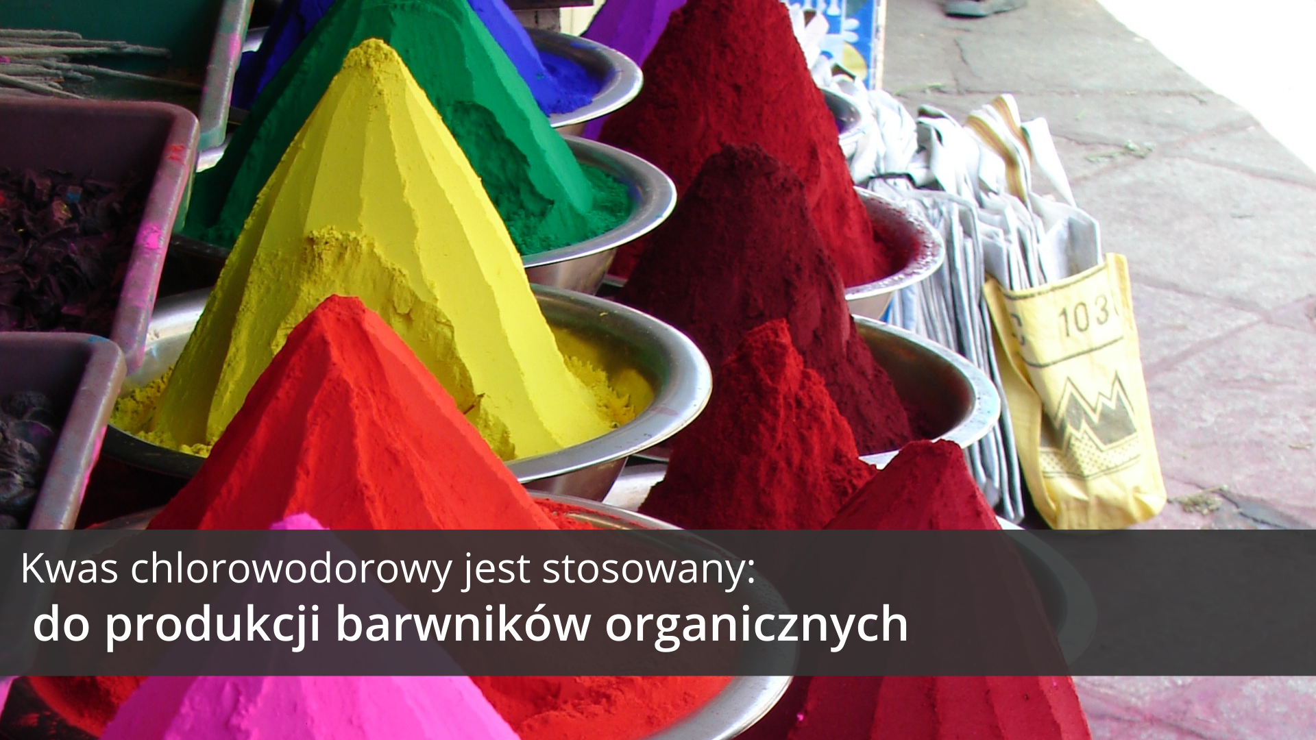 Szósta ilustracja galerii przedstawia zdjęcie fragmentu bazaru, na którym sprzedawane są pigmenty i barwniki. W ustawionych obok siebie dwóch rzędach metalowych misek, usypane są kolorowe pagórki barwników w najróżniejszych odcieniach. W tle widać płyty chodnikowe świadczące o tym, że jest to targowisko uliczne. Na tle obrazka, w dolnej części ilustracji, znajduje się ciemnoszary pasek, na którym umieszczono jasny napis: Kwas chlorowodorowy jest stosowany do produkcji barwników organicznych.