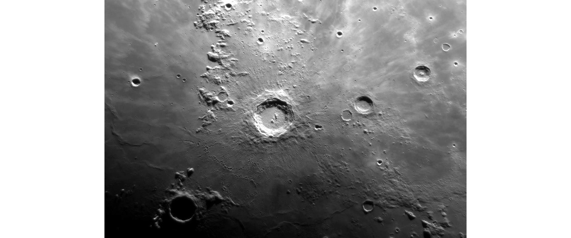 Na zdjęciu widoczna jest powierzchnia Księżyca – jej ciemnoszary wycinek w kształcie kwadratu. W centralnej części widoczny jest duży krater otoczony przez mniejsze rozrzucone w dowolny sposób wokół niego.