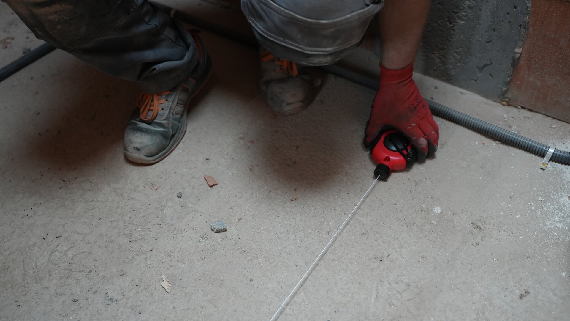 Na grafice przedstawiono kucającego pracownika, który za pomocą sznurka traserskiego do wyznaczenia prostych linii na betonie.