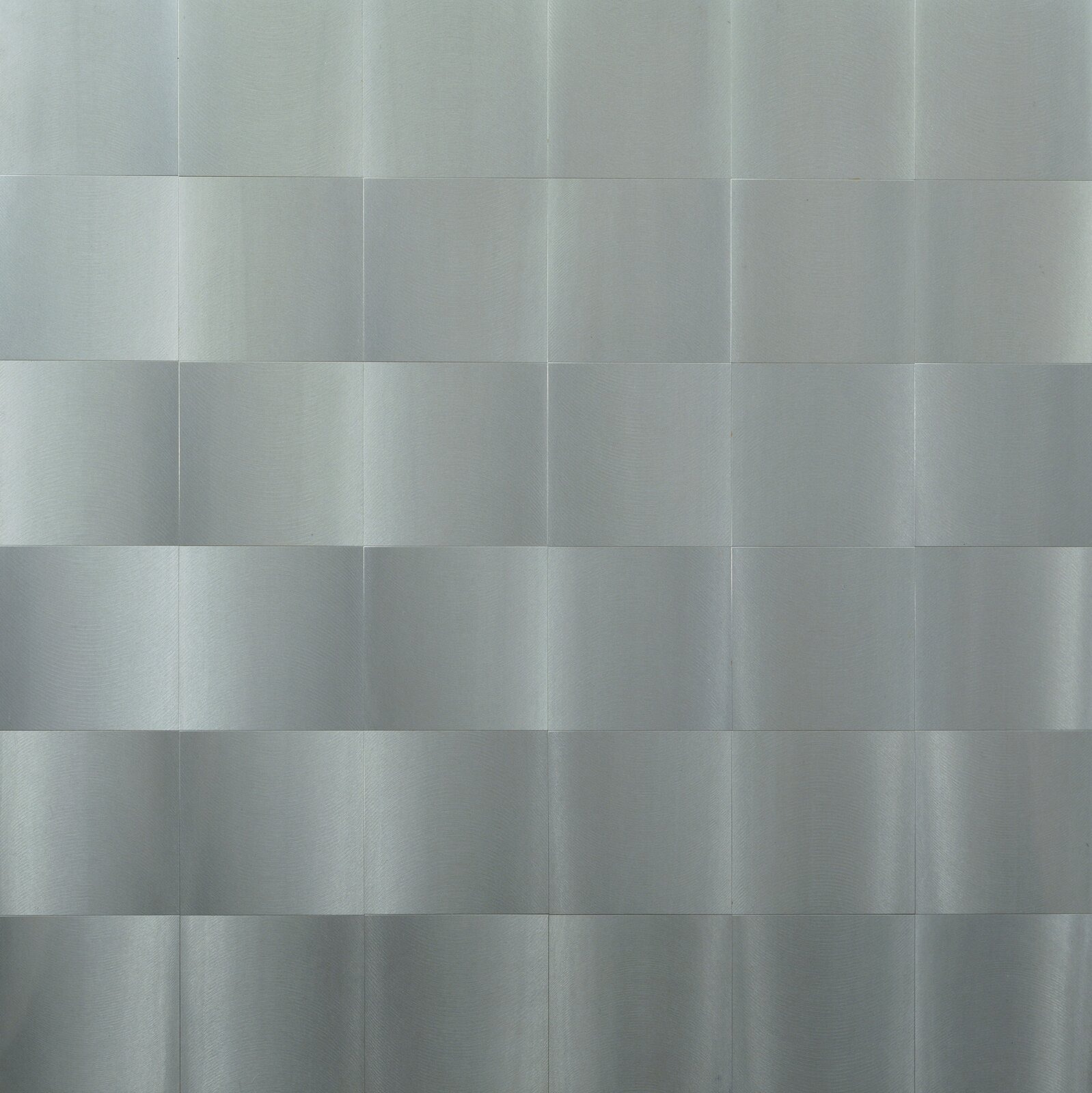 Zdjęcie przedstawia rzeźbę o płaskiej powierzchni złożonej z aluminiowych kwadratowych blaszek, ułożonych jedna obok drugiej. Dzięki szczotkowaniu powierzchni blaszek, zyskały one wzorzystą fakturę, a ułożone razem łączą się w fale. Światło odbijające się od blaszek tworzy efekt trójwymiarowości, jakby rzeźba była wypukła.