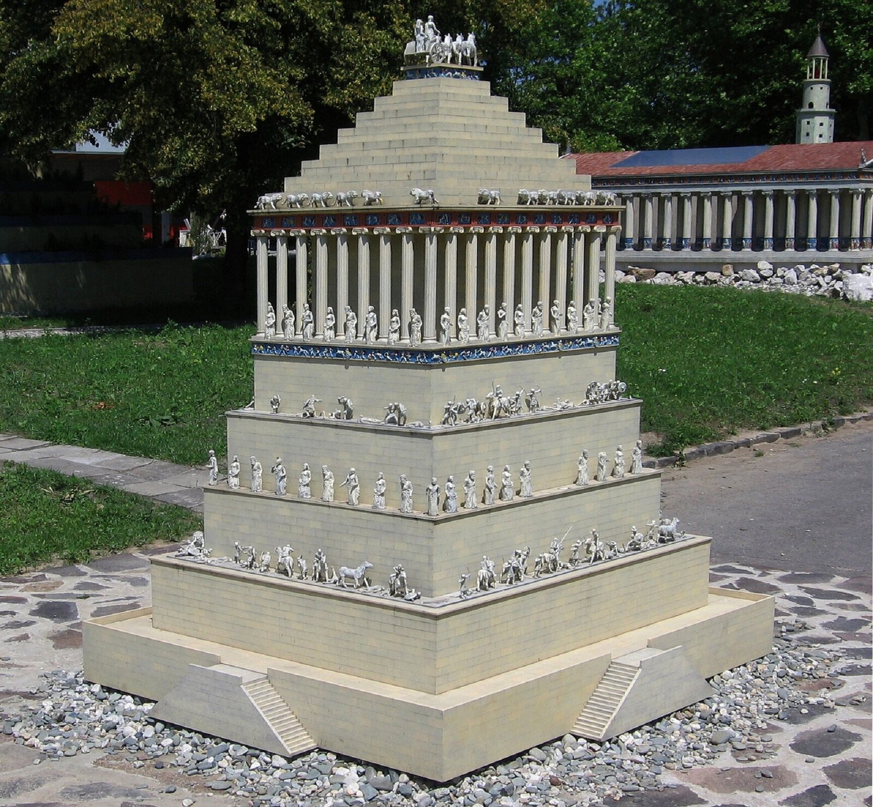 Ilustracja przedstawia zdigitalizowany obraz ukazujący Mauzoleum w Halikarnasie. Mauzoleum zaliczane jest do siedmiu cudów świata. Budowla została zaprojektowana przez architektów Satyrosa i Pyteosa. Budynek nie przetrwał do dzisiejszych czasów. Jego wysokość sięgała 45 metrów. Na fotografii widzimy świątynię z czterdziestoma kolumnami. Na jej szczycie znajduje się dwudziestocztero stopniowa piramida. Na każdym poziomie budowli znajdują się liczne rzeźby i posągi. Dookoła Mauzoleum możemy dostrzec kamienną drogę.