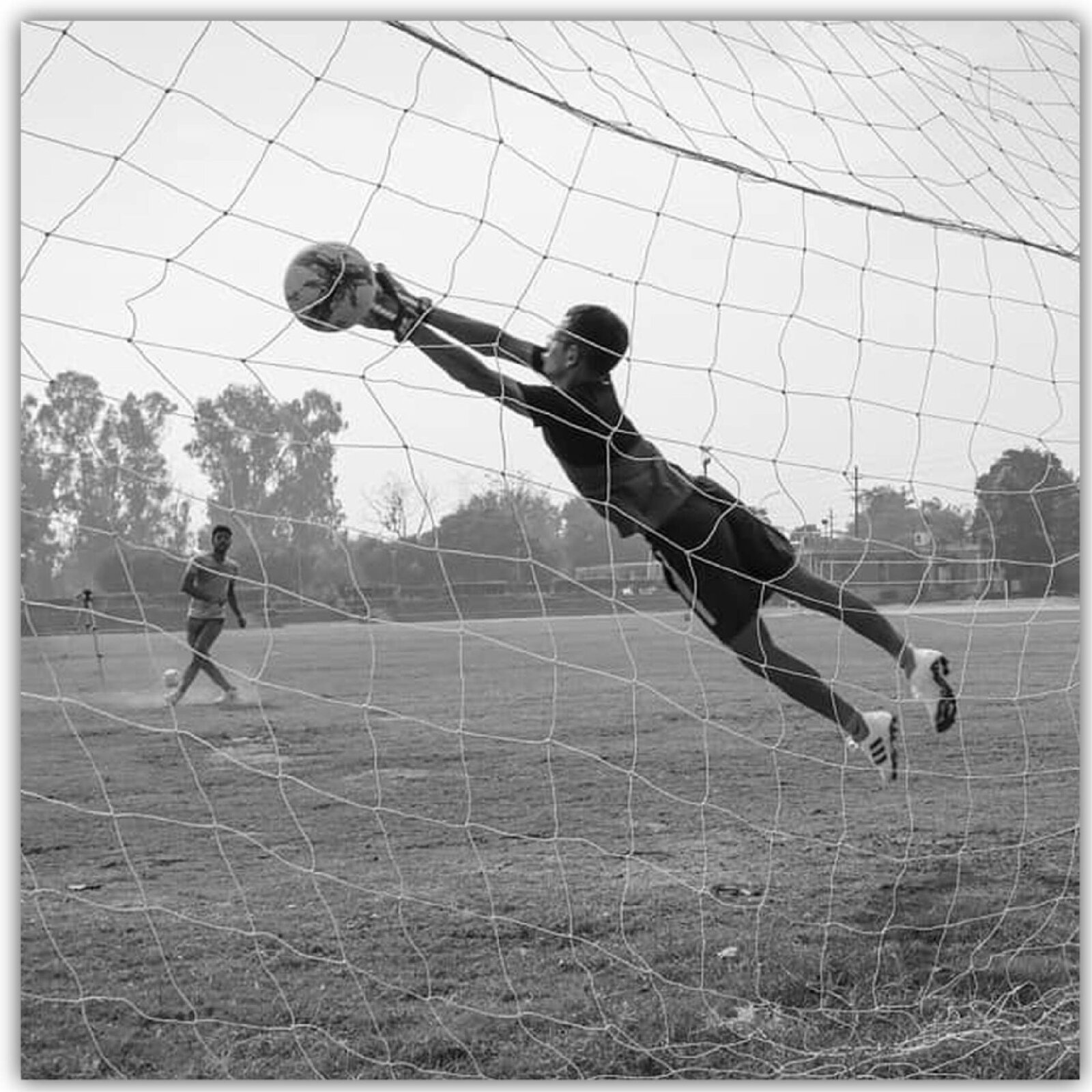 Ilustracja przedstawia chłopaków grających w piłkę nożną. Jeden ukazany jest w bramce podczas obrony. Drugi przymierza się do strzału.