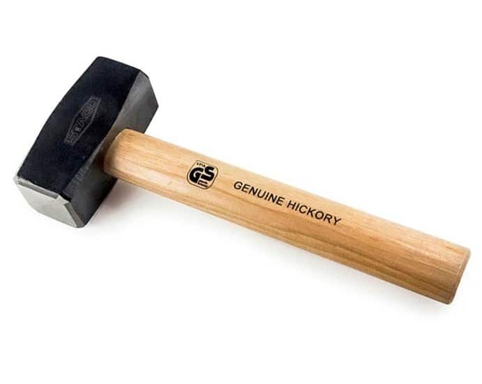 Grafika przedstawia młotek. Narzędzie składa się z czarnego obucha i jasnobrązowego trzonka.