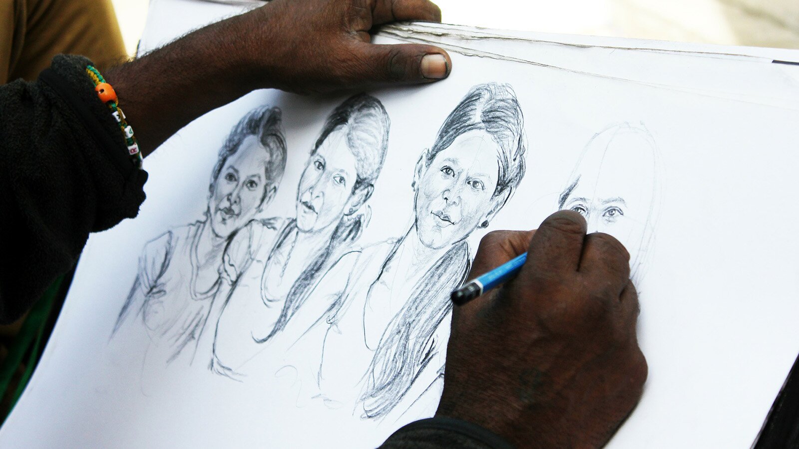 Zdjęcie przedstawia osobę, która szkicuje ołówkiem portret kobiety. 