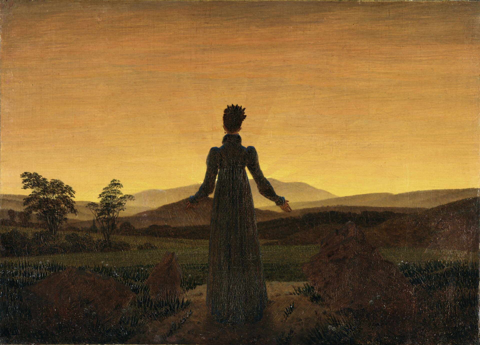 Obraz przedstawia kobietę stojącą na ścieżce biegnącą przez pola. Kobieta jest odwrócona tyłem do widza. Jest w długiej sukni. Ma rozłożone ręce. Naprzeciw niej widać wzgórza i zachodzące słońce.