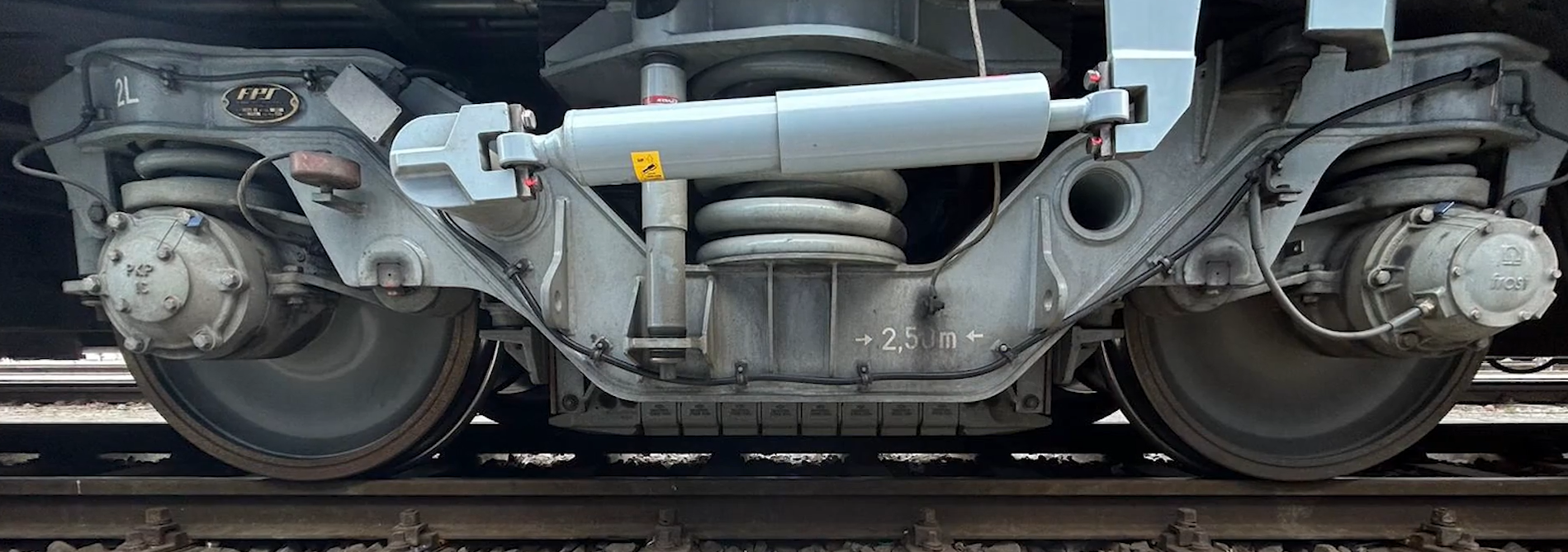 Zdjęcie przedstawia hamulec szynowy. Widoczny jest wózek napędny z boku. Na środku, pomiędzy zestawami kołowymi, nad szyną zawieszony jest podłużny element podzielony na osiem segmentów.