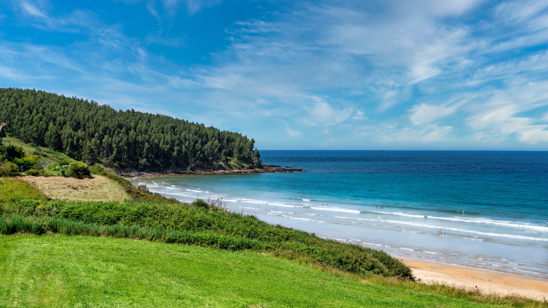 Zdjęcie przedstawia wybrzeże Asturii. Zielony, zalesiony teren przy plaży nad morzem.
