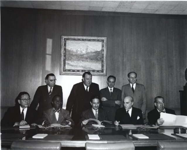 Kliknij żeby powiększyć Na zdjęciu utrwalono moment podpisania Konwencji ONZ w sprawie Zapobiegania i Karania Zbrodni Ludobójstwa z roku 1948. W pomieszczeniu znajduje się 9 mężczyzn, w tym jeden ciemnoskóry. 5 z nich siedzi przy dużym stole, za nimi stoi 4 innych mężczyzn. Pierwszy z prawej to Rafał Lemkin. Wśród 5 siedzących mężczyzn, ten będący w środku, trzyma w ręku tekst Konwencji i czyta go. Za mężczyznami znajduje się ściana wyłożona drewnem, a na niej wisi obraz z górskim pejzażem.