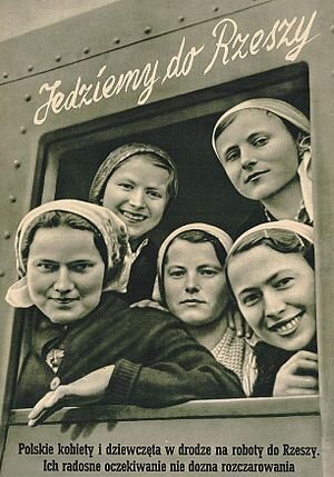 Ilustracja przedstawia uśmiechnięte młode kobiety w wagonie pociągu. Na górze napis: Jedziemy do Rzeszy. Dolny: Polskie kobiety i dziewczęta w drodze na roboty do Rzeszy. Ich radosne oczekiwanie nie dozna rozczarowania.