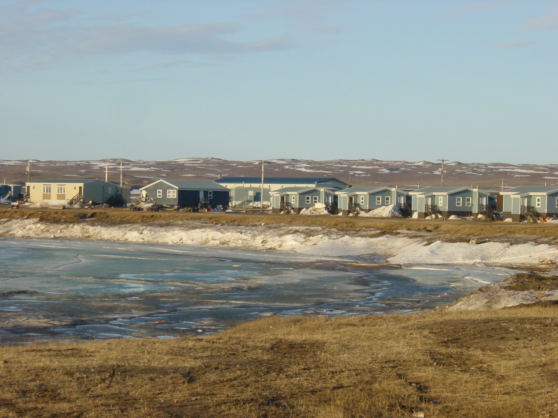 Na zdjęciu osiedle parterowych domów. Zbudowane zostało nad brzegiem zamarzniętego zbiornika wodnego.  