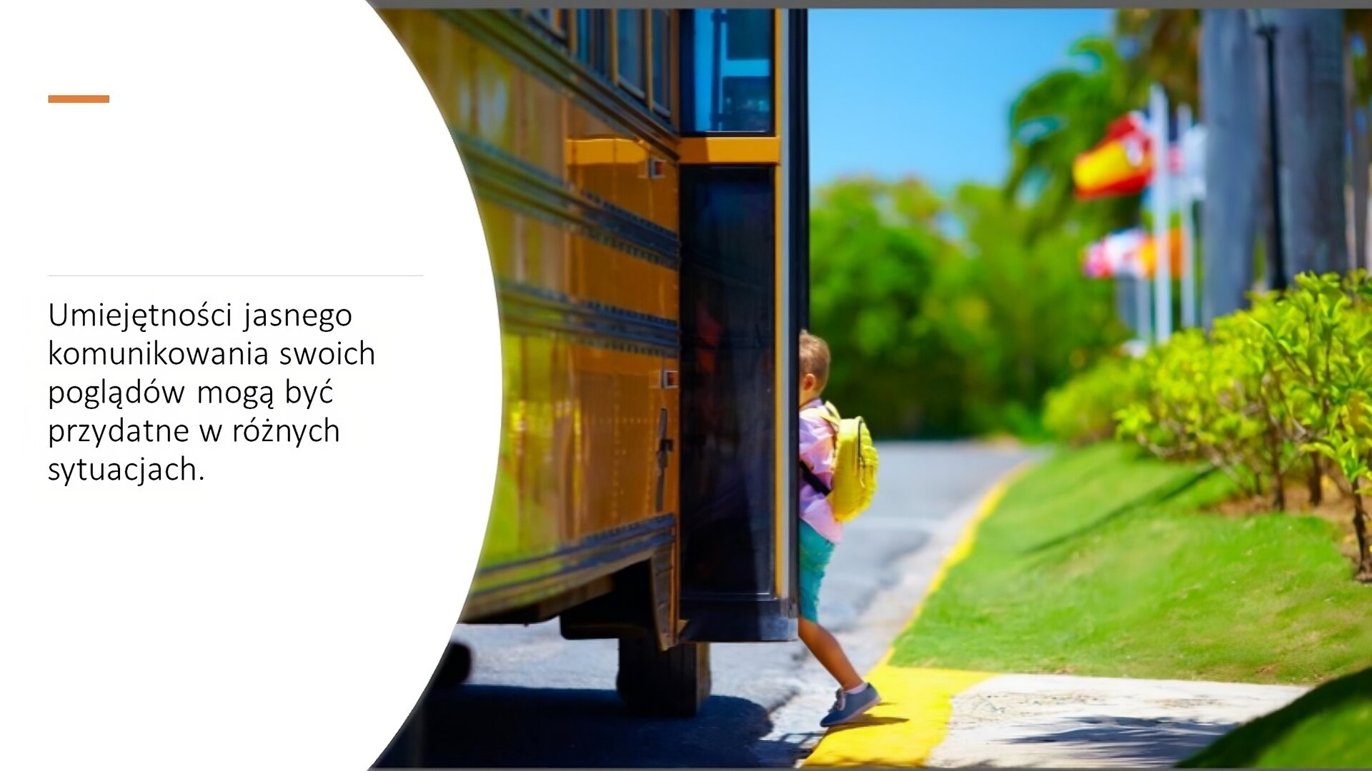 Biały slajd. Z lewej strony tekst: „Umiejętności jasnego komunikowanie swoich poglądów mogą być przydatne w różnych sytuacjach”. Obok, z prawej strony slajdu, zdjęcie przedstawiające małego chłopca, który wchodzi do żółtego autobusu szkolnego. Za nim zielona trawa i krzewy, a w tle kolorowe flagi powiewające na wietrze.
