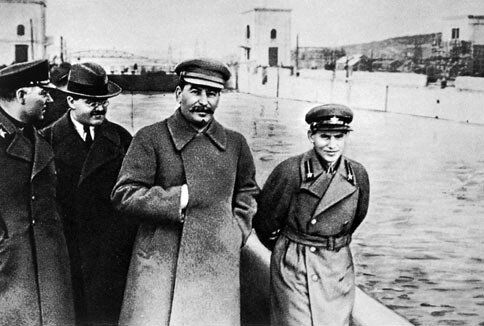 Kliknij, aby powiększyć Zdjęcie przedstawia sylwetki czterech mężczyzn. Wśród nich jest Józef Stalin. Ubrany jest w płaszcz, prawą rękę trzyma włożoną między zapięcia płaszcza, na wysokości klatki piersiowej. Pozostali mężczyźni są ubrani: pierwszy od lewej jest w wojskowy płaszcz, drugi w płaszcz. Ostatni niski mężczyzna, którym jest Nikołaj Jeżow, ubrany jest w mundur wojskowy a ręce ma założone do tyłu. Obok przepływa woda, w tle widać zabudowania i most.