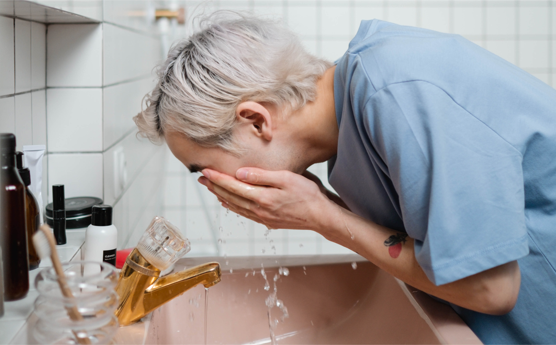 Zdjęcie przedstawia chłopaka wykonującego poranną higienę. Chłopak myje twarz nad umywalką w łazience.