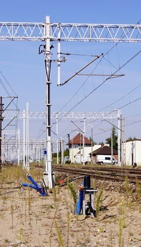 Ilustracja przedstawia przewody zasilaczy prowadzone po słupie trakcyjnym.