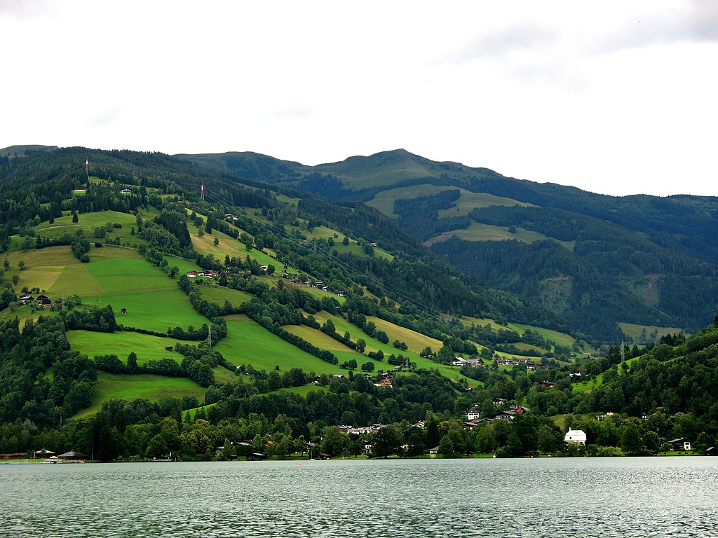 Ilustracja przedstawia wieś w Austrii, osadzoną na wzgórzach. Między lasami znajdują się gospodarstwa domowe.