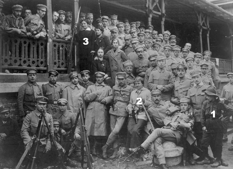 Zdjęcie przedstawia sporą grupę ludzi. To oddział Strzelców na krakowskich Oleandrach. Poza umundurowanymi jest też kilka kobiet. Pozują na werandzie. Panuje spokojna atmosfera. 
