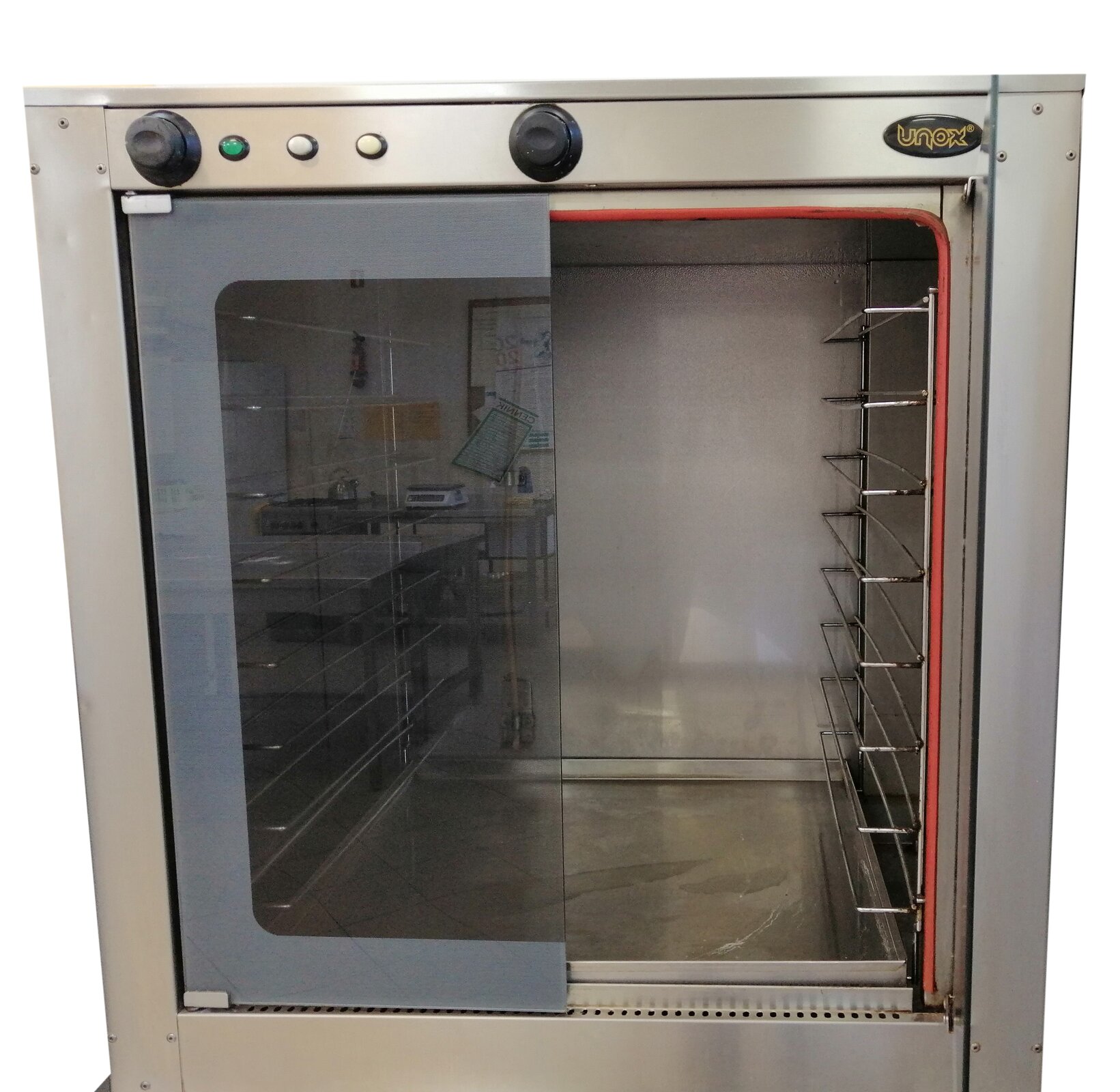 Zdjęcie przedstawia komorę rozrostową. Widoczny jest przód urządzenia o kwadratowym kształcie z obudową ze stali, drzwiczkami z półprzeźroczystym szkłem osadzonym w szarej ramie. W górnej części obudowy widoczne są pokrętła i włączniki. Wewnątrz komory widoczne są po prawej stronie metalowe pręty służące do wsuwania w nie blachy.