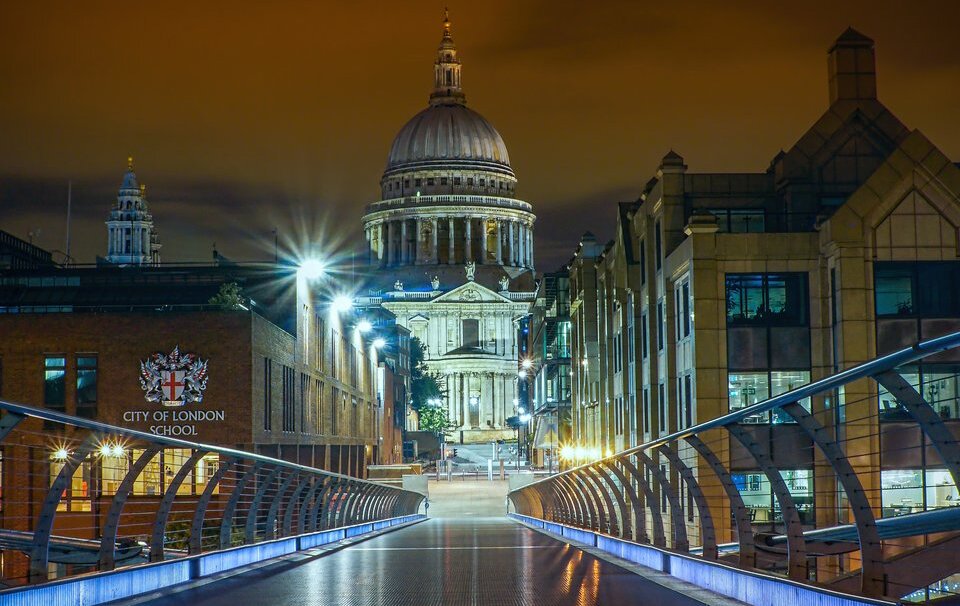 Fotografia przedstawia most milenijny u dołu, z którego zostało zrobione zdjęcie. W centrum widać katedrę świętego Pawła. Wysoka budowla jest zbudowana z jasnego kamienia, zakończona kopułą, na której widać mniejszą wierzę.
