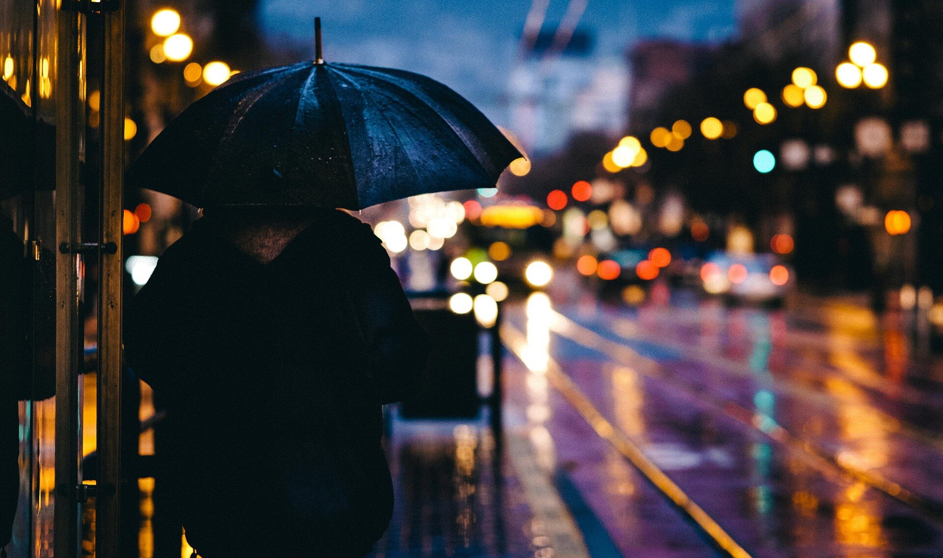 Zdjęcie przedstawia człowieka, który stoi przy ruchliwej ulicy w nocy. Trzyma w ręce parasol. Zadanie alternatywne wyświetla się w trybie dostępności.