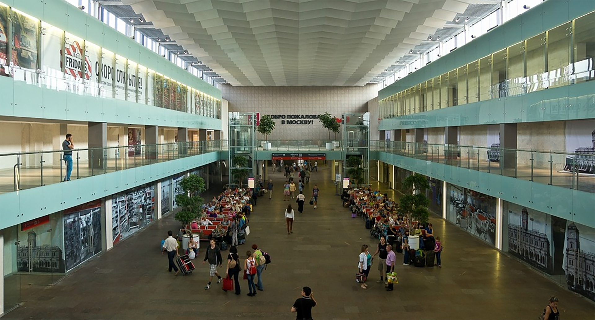 Ilustracja przedstawia wnętrze poczekalni z pasażerami. Wokół widać piętra budynku.