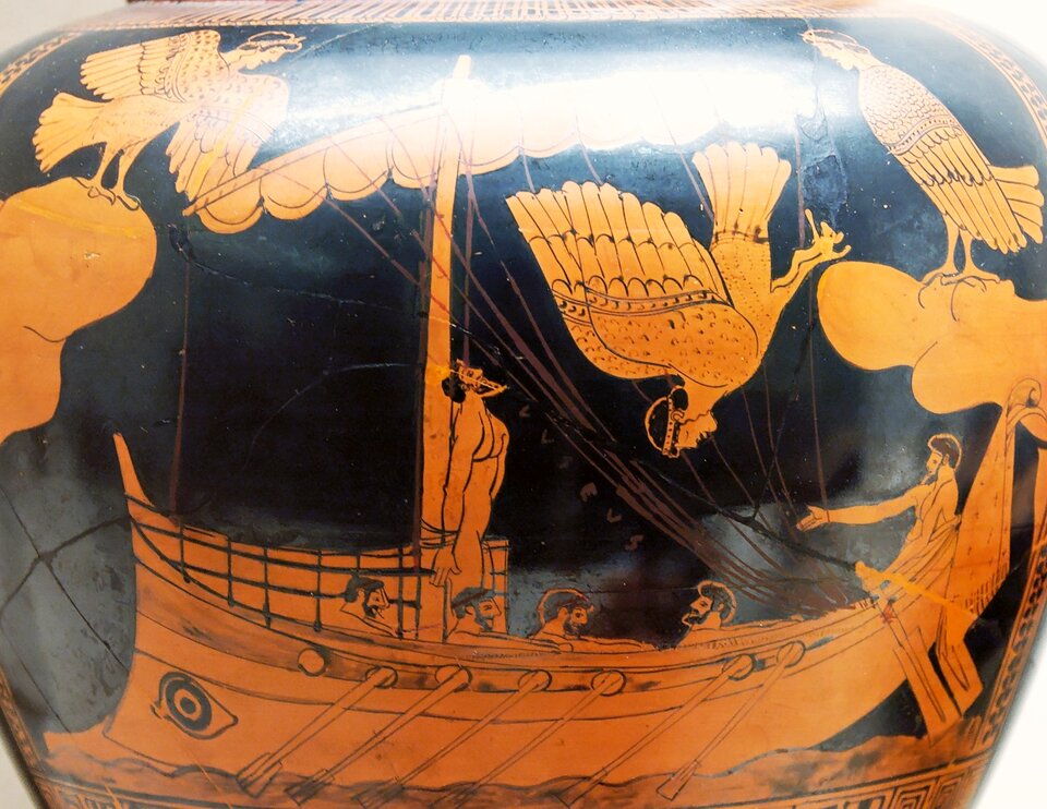 Zdjęcie przedstawia starożytną wazę z czarno-pomarańczowym malunkiem. Prezentuje on płynący okręt. Do masztu przywiązany jest nagi mężczyzna. Kilku mężczyzn wiosłuje. Nad statkiem unoszą się syreny, które mają postać pół kobiety pół ptaka.