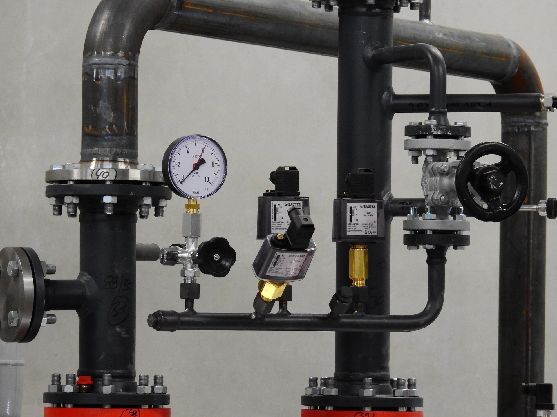 Rys. a. Na zdjęciu znajduje się instalacja wodna z rurami o różnej grubości połączonymi ze sobą, do których podłączono ciśnieniomierz – przyrząd z okrągłą tarczą z podziałką i wskazówką, która może obracać się na tle tarczy.