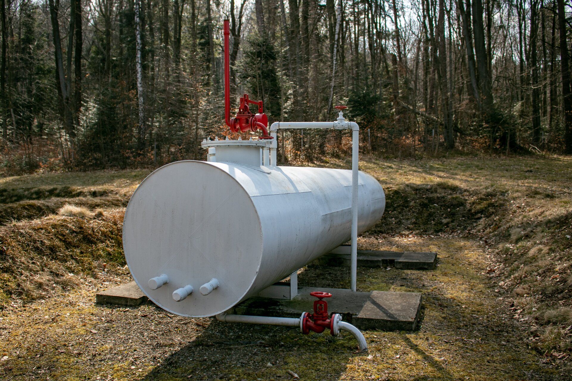 Na zdjęciu widać zbiornik napowierzchniowy cylindryczny przeznaczony do magazynowania ropy naftowej sześciu, który umieszczony jest na stalowych nogach w niewielkim zagłębieniu w ziemi tak zwanym obwałowaniu. Na górze zbiornika znajduje się zawór bezpieczeństwa. Zawór ten jest elementem instalacji służącym do zabezpieczenia układu przed nadmiernym wzrostem ciśnienia. Zawór bezpieczeństwa jest w kształcie odwróconej czerwonej fajki. Przy podstawie zbiornika znajduje się zawór spustowy wyposażonym w dwa czerwone pokrętła. Za zbiornikiem znajduje się kolejny podobny zbiornik napowierzchniowy. Z prawej strony zdjęcia widać niewielkie dwukondygnacyjny obiekt budowlany o białej ścianie oraz dachu wykonanym z brązowej blachy falistej.