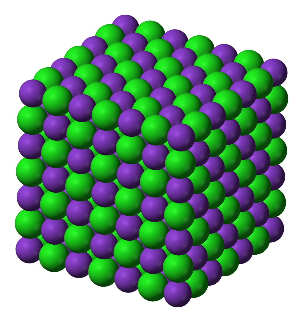 Ilustracja przedstawia kryształ jonowy chlorku sodu, w którym kationy potasu (fioletowe kulki) i aniony chlorkowe (zielone kulki) są ułożone naprzemiennie i tworzą sześcian.