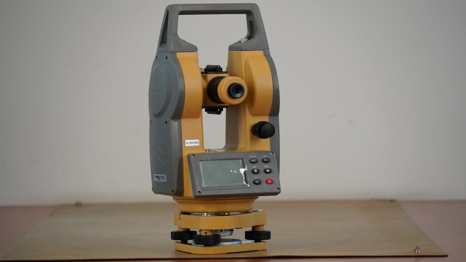 Na zdjęciu przedstawiono teodolit. Urządzenie posiada trójkątną podstawę w formie płytki sprężynującej. W każdym jej rogu znajduje się śruba poziomująca. Na śrubach osadzona jest spodarka, czyli podstawa instrumentu. W spodarce mieści się śruba dociskowa, a na spodarce okrągła alidada, czyli korpus urządzenia. Na nim zaś znajdują się pokrętła leniwki alidady i leniwki lunety oraz zacisk alidady i lunety. Konstrukcję instrumentu uzupełnia prostokątna rama z uchwytem w górnej części, wewnątrz została osadzona luneta. Pod obiektywem znajduje się wyświetlacz.