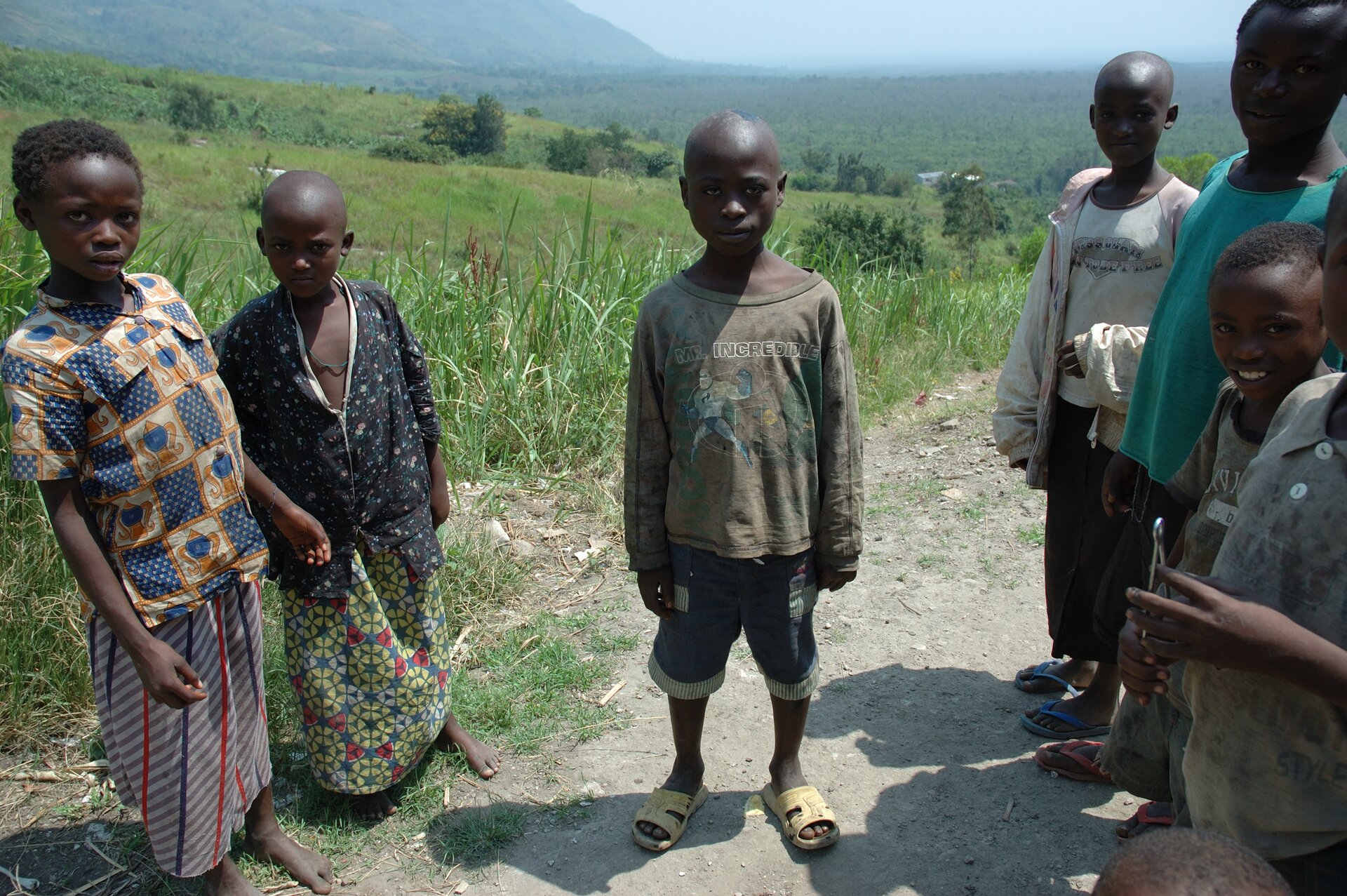 Na zdjęciu znajduje się kilka ciemnoskórych osób z grupy społecznej Hutu zamieszkującej Rwandę. Kobiety są ubrane w długie spódnice i kolorowe bluzki, mężczyźni mają ogolone głowy, są ubrani w krótkie spodenki i koszulki. 
