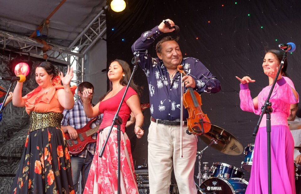 Ilustracja przedstawia zespół romski podczas koncertu. Ukazuje ona muzyków tańczących na scenie. Kobiety ubrane są w długie spódnice w kolorach róży, pomarańczy i bieli. Artysta wokalny trzyma w ręce skrzypce a w drugiej mikrofon. Ubrany jest w fioletową koszulę z białymi zdobieniami oraz jasne spodnie.