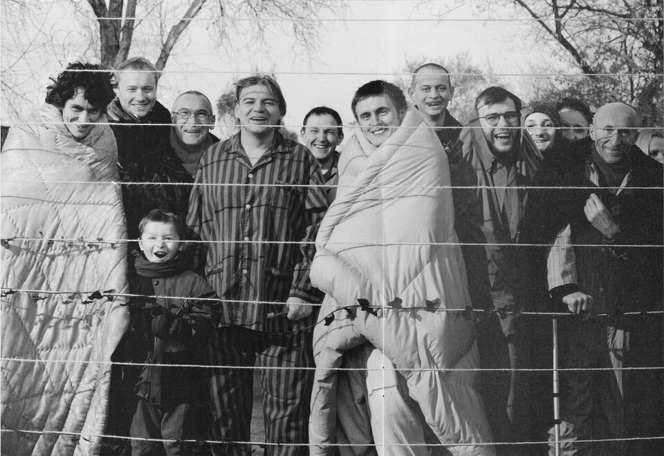 Zbigniew Libera, „Mieszkańcy” z cyklu „Pozytywy”. Na ilustracji widoczne są osoby: mężczyźni i kobiety oraz dziecko, niektóre osoby ubrane są w więzienne pasiaki. Stoją za rozpiętymi sznurkami i śmieją się.