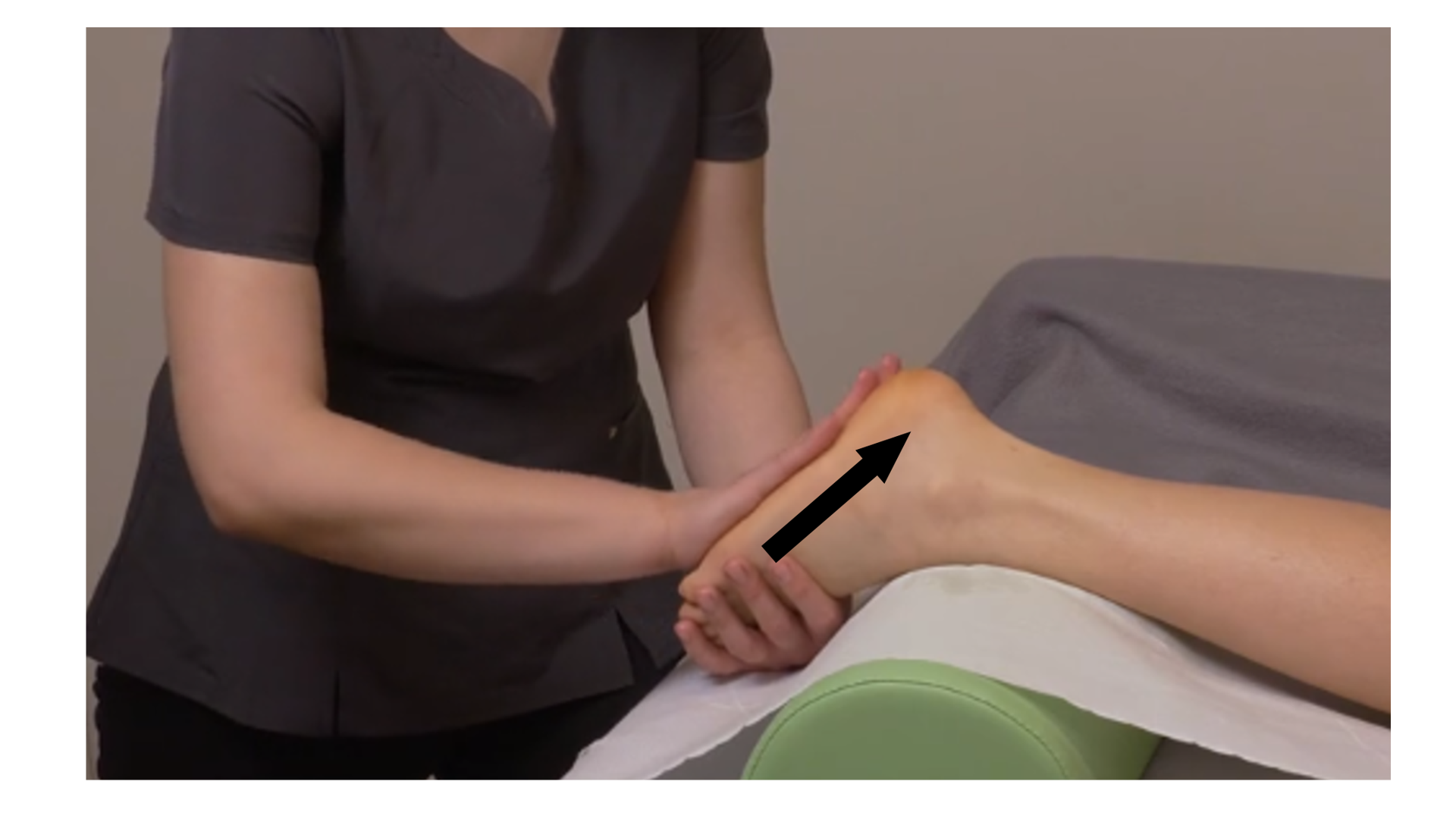 Zdjęcie pod tytułem głaskanie powierzchowne i głębokie podeszwowej strony stopy. Zdjęcie przedstawia masażystkę trzymającą jedną ręką ułożoną na wałku stopę pacjentki. Druga ręka masażystki wykonuje posuwiste ruchy od palców do pięty po podeszwowej stronie stopy. 