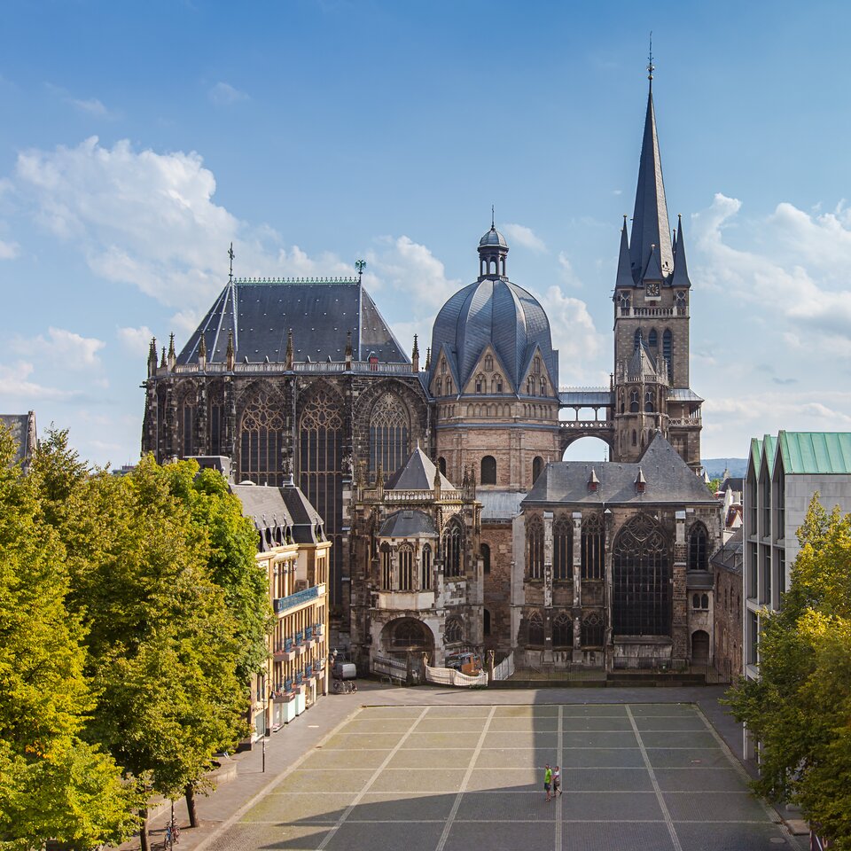 lustracja przedstawia kaplicę pałacową w Akwizgranie. Bryła kaplicy jest ledwie widoczna pośród elementów gotyckiej katedry. Kaplica jest wysoką, trójkondygnacyjną budowlą z jednakowymi otworami okiennymi na każdej kondygnacji. Całość jest przykryta bardzo wysoką, wydłużoną kopułą z wyraźnymi wzdłużnymi, oktagonalnymi podziałami. Na szczycie umieszczona jest latarnia.