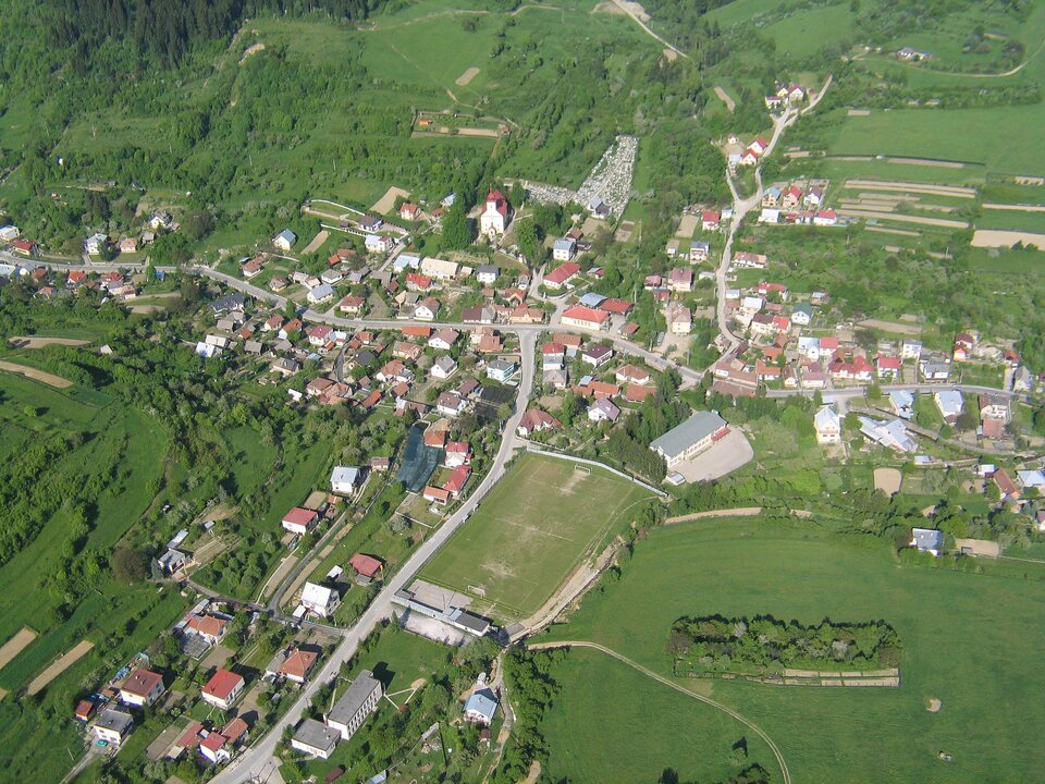 Przykład lotniczego zdjęcia nachylonego. Punkt wykonania zdjęcia i ukazana perspektywa wskazuje na nachylenie aparatu wobec obiektu pod kątem powyżej 3 stopni. Na fotografii uchwycone krzyżujące się drogi, budynki oraz obiekty zielone, lasy i łąki.  