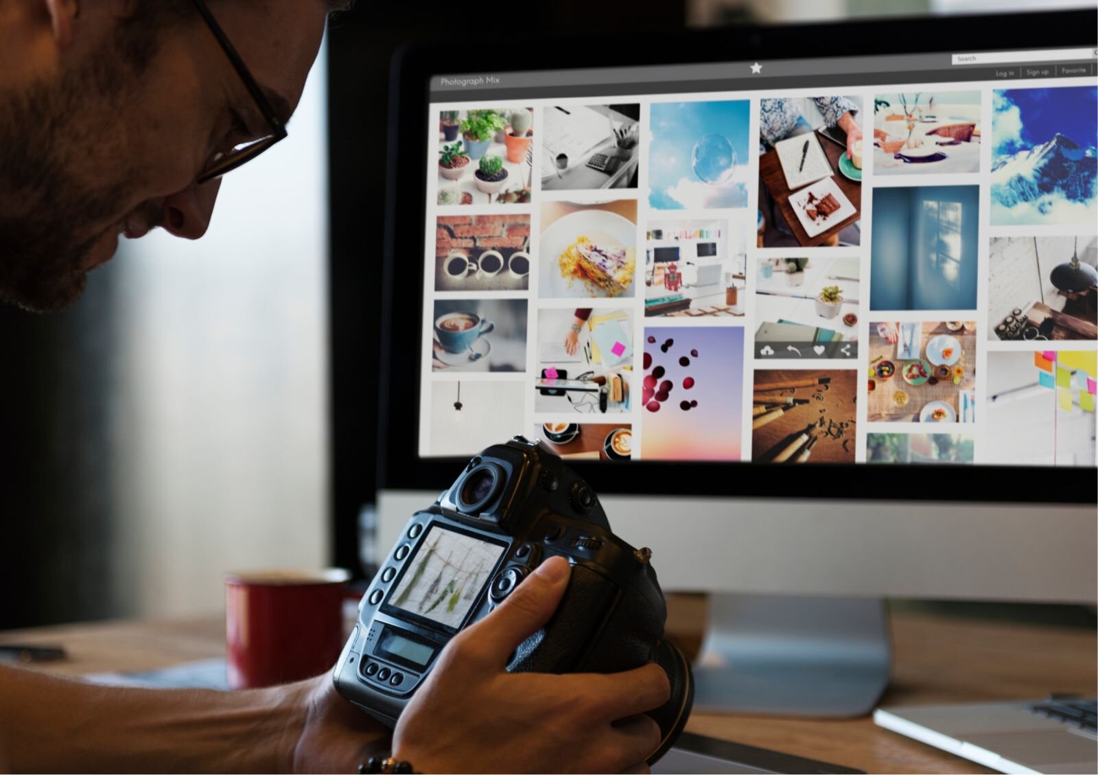 Zdjęcie ukazuje fotografa sprawdzającego na aparacie cyfrowym zrobione wcześniej zdjęcia. Fotograf siedzi przed biurkiem trzymając w ręku aparat, uśmiecha się. Przed nim stoi monitor, na ekranie są zrzucone zdjęcia. 