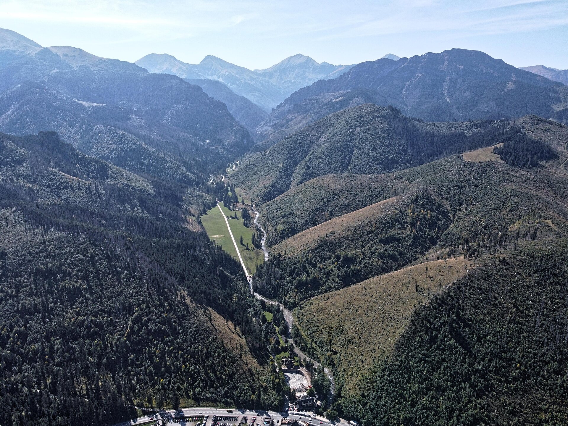 Na fotografii krajobraz górski. Jest to dolina w której znajduje się prosta ścieżka. Po bokach doliny wnoszą się góry porośnięte lasem. Stoki gór na pierwszym planie są łagodniejsze niż stoki gór znajdujących się w oddali. 