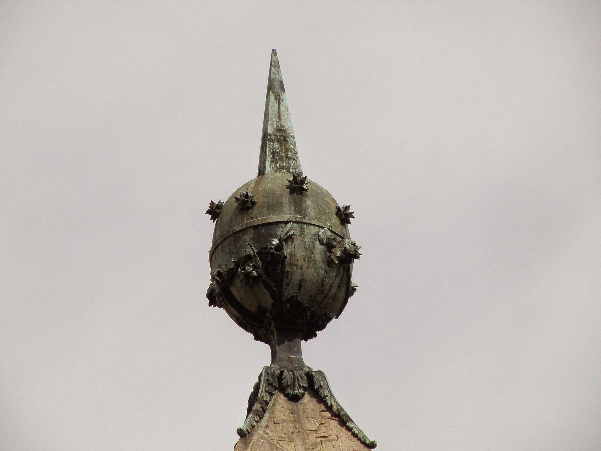 Fotografia przedstawia zakończenie dachu - okrągły, metalowy posąg z wychodzącym od niego szpikulcem.