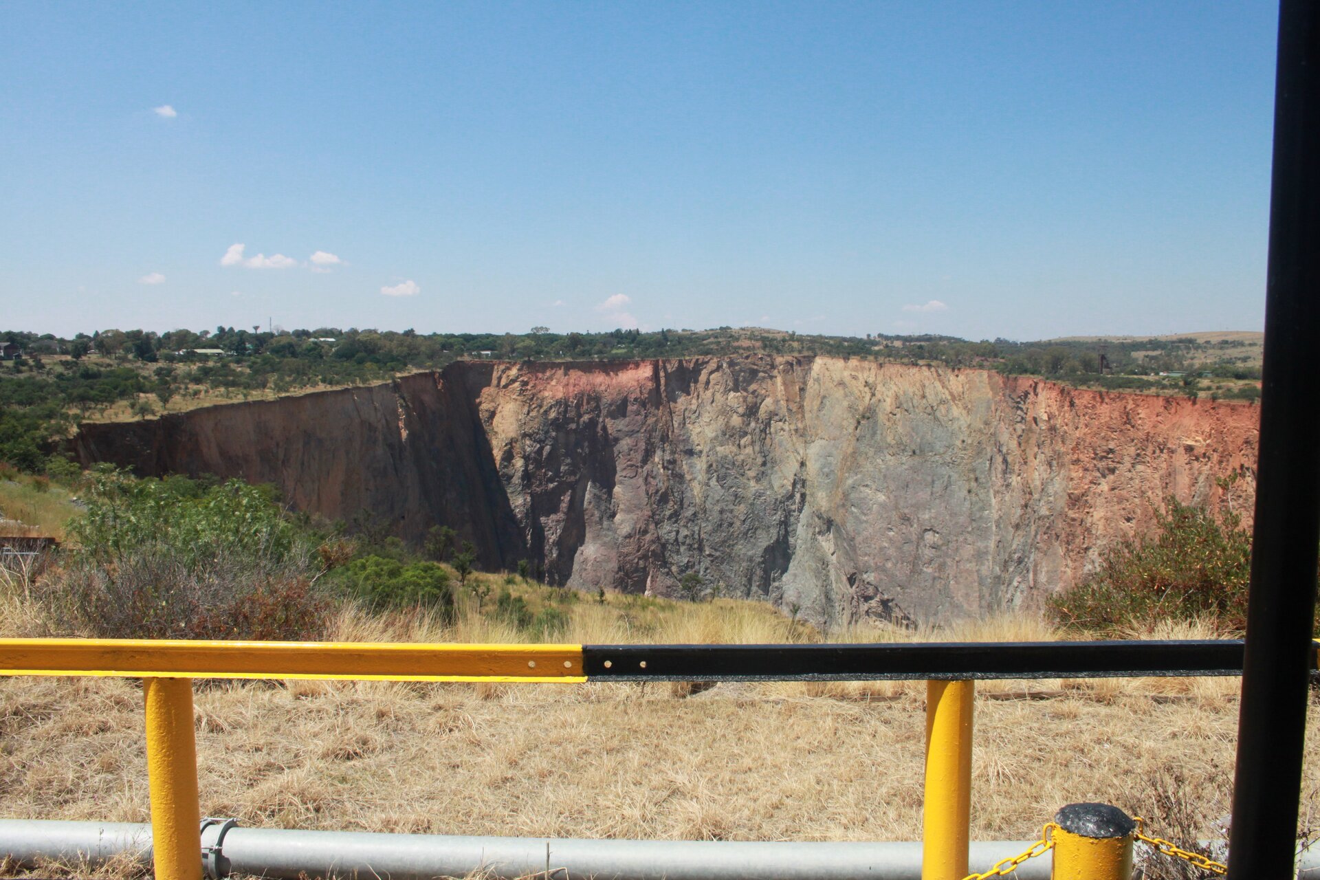 Zdjęcie wykonane nad wyrobiskiem odkrywkowej kopalni. Otoczone barierkami. Wyrobisko o bardzo dużej głębokości i średnicy, niemal pionowe ściany, nie jest ukazane jego dno. Dookoła płaski teren.