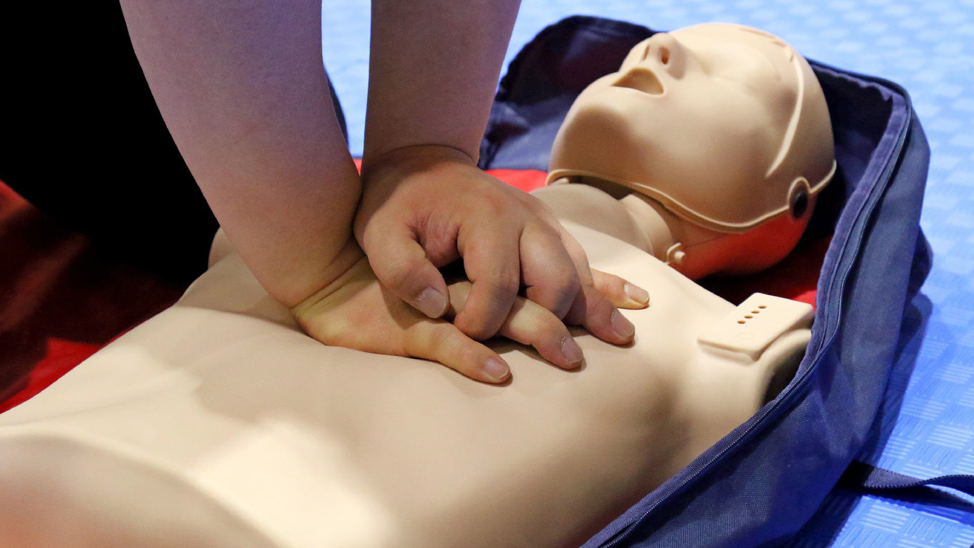 Zdjęcie przedstawia fantoma, manekina do ćwiczenia udzielania pierwszej pomocy. Na klatce piersiowej manekina ułożone są czyjeś dłonie przygotowane do masażu serca.