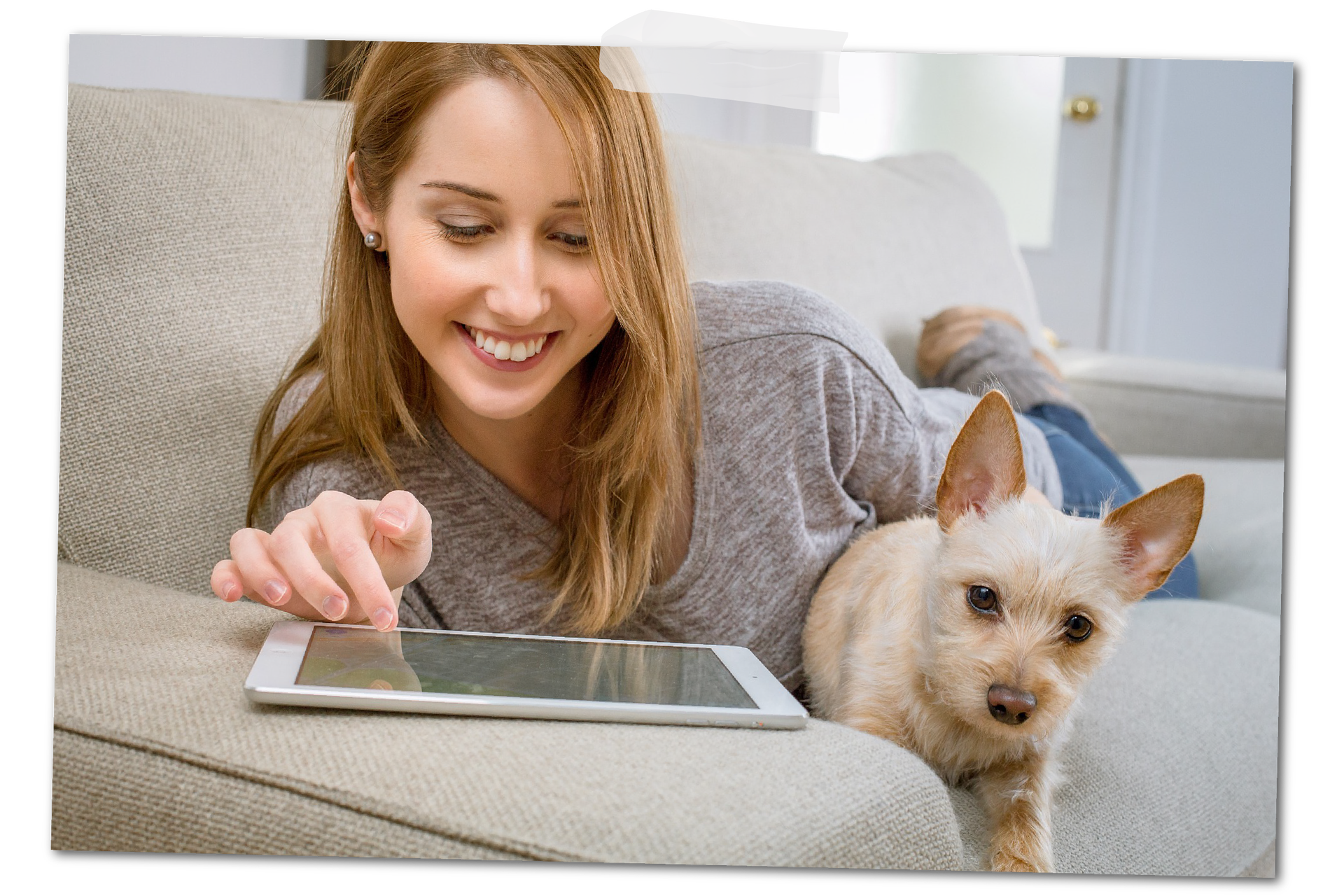 Zdjęcie przedstawia młodą kobietę leżącą na kanapie z małym, kremowym pieskiem. Kobieta ogląda coś na tablecie uśmiechając się.