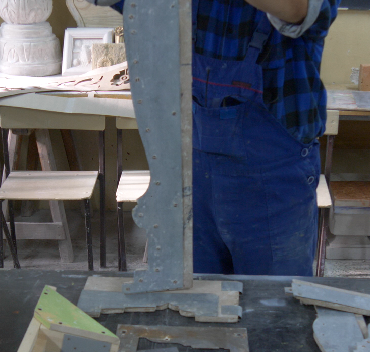 Zdjęcie przedstawia wykrój do belek i podciągów. Pracownik w stroju roboczym przytrzymuje wykrój w pionie. Wykrój po jednej stronie ma nieregularny kształt potrzebny do wykonania zdobienia.