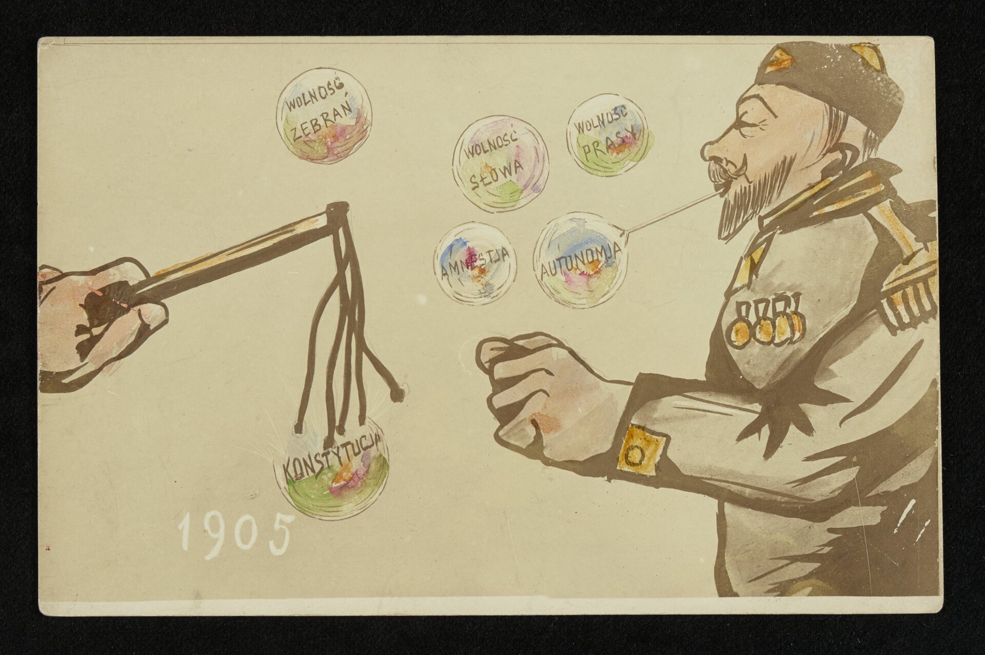 Rysunek przedstawia mężczyznę w mundurze wojskowym z licznymi orderami. Mężczyzna wydmuchuje banki mydlane z napisami: autonomia, wolność zebrań, wolność prasy, wolność słowa, amnestia. Po lewej stronie rysunku jest dłoń trzymająca bicz. Dotyka on bańki mydlanej z napisem: Konstytucja. Na rysunku jest podany rok 1905.   