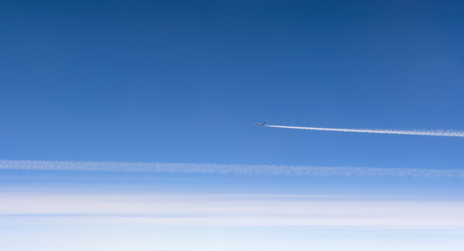 Fotografia przedstawia samolot lecący po błękitnym niebie, nad chmurami. Za samolotem ciągnie się biały ślad.