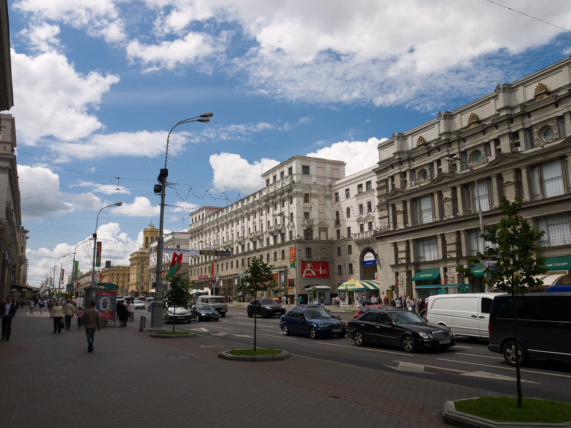 Zdjęcie przedstawia szeroką, reprezentacyjną ulicę stolicy Białorusi – Mińska. Piękne, zdobione kamienice. Na kilkupasmowej jezdni samochody, po szerokich chodnikach spacerują ludzie.