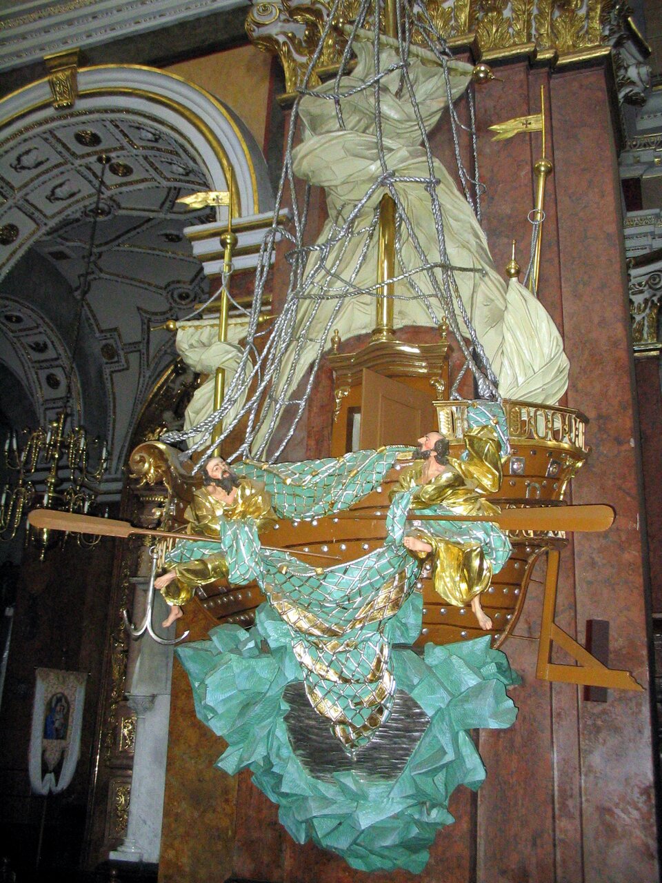 Po prawej stronie widoczna kazalnica z kościoła św. Teresy w Przemyśluwyrzeźbiona w drewnie w formie trójmasztowego okrętu. Ukazana jest jako usadowiona naskale, z ogromnym żaglem miotanym gwałtownym wiatrem, który tworzy baldachim. Mapostać okrętu o dwóch pokładach, uzbrojonego w działa z kotwicą przy dziobie i sterem narufie. Maszt zwieńczony banderą z krzyżem  podtrzymuje przechyloną reję. Takielunek z linjest bardzo rozbudowany. Na niższym z pokładów ustawione zostały dwa wyobrażeniaświętych Piotra i Pawła wydobywających z morza sieć wypełnioną rybami.