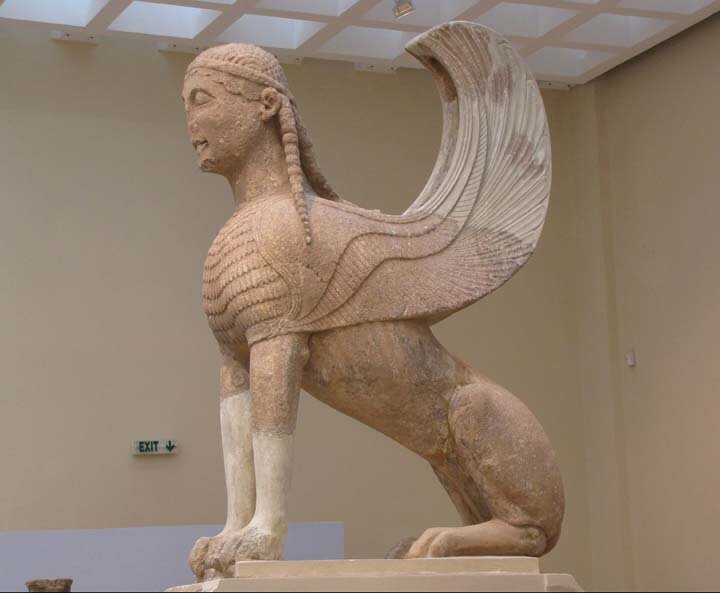 Na zdjęciu znajduje się kamienny pomnik sfinksa. Jest to mityczne stworzenie o tułowiu lwa, głowie człowieka o długich włosach i skrzydłach. 