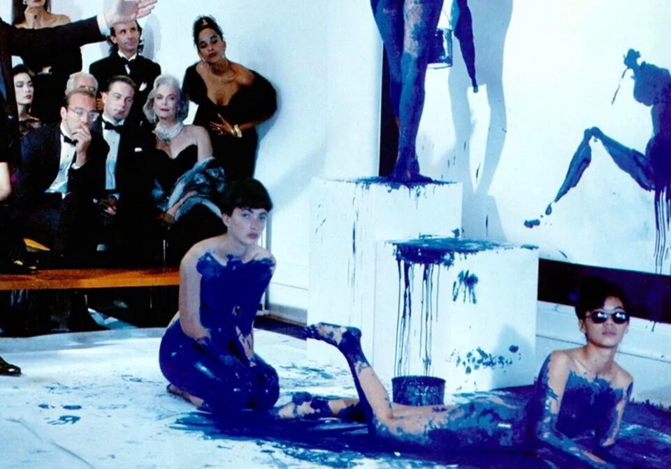 Ilustracja przedstawia performance Yves Klein "Antropometrie". Na zdjęciu wykonanym we wnętrzu, z lewej strony znajduje się publiczność  w eleganckich strojach. W centrum na białym płótnie rozłożonym na podłodze znajdują się dwie nagie modelki pomalowane jednolitym kolorem intensywnego błękitu zbliżonego do ultramaryny. Jedna modelka leży, druga siedzi obok. W tle jest biała ściana, na której znajdują się plamy niebieskiej farby przypominające sylwetkę kobiecą. 