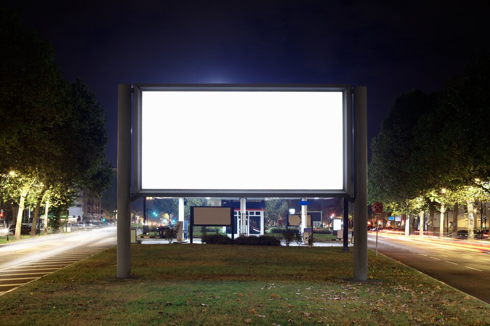 Ilustracja przedstawia podświetlony billboard (bez żadnej reklamy), umieszczony w pasie zieleni pomiędzy jezdniami.