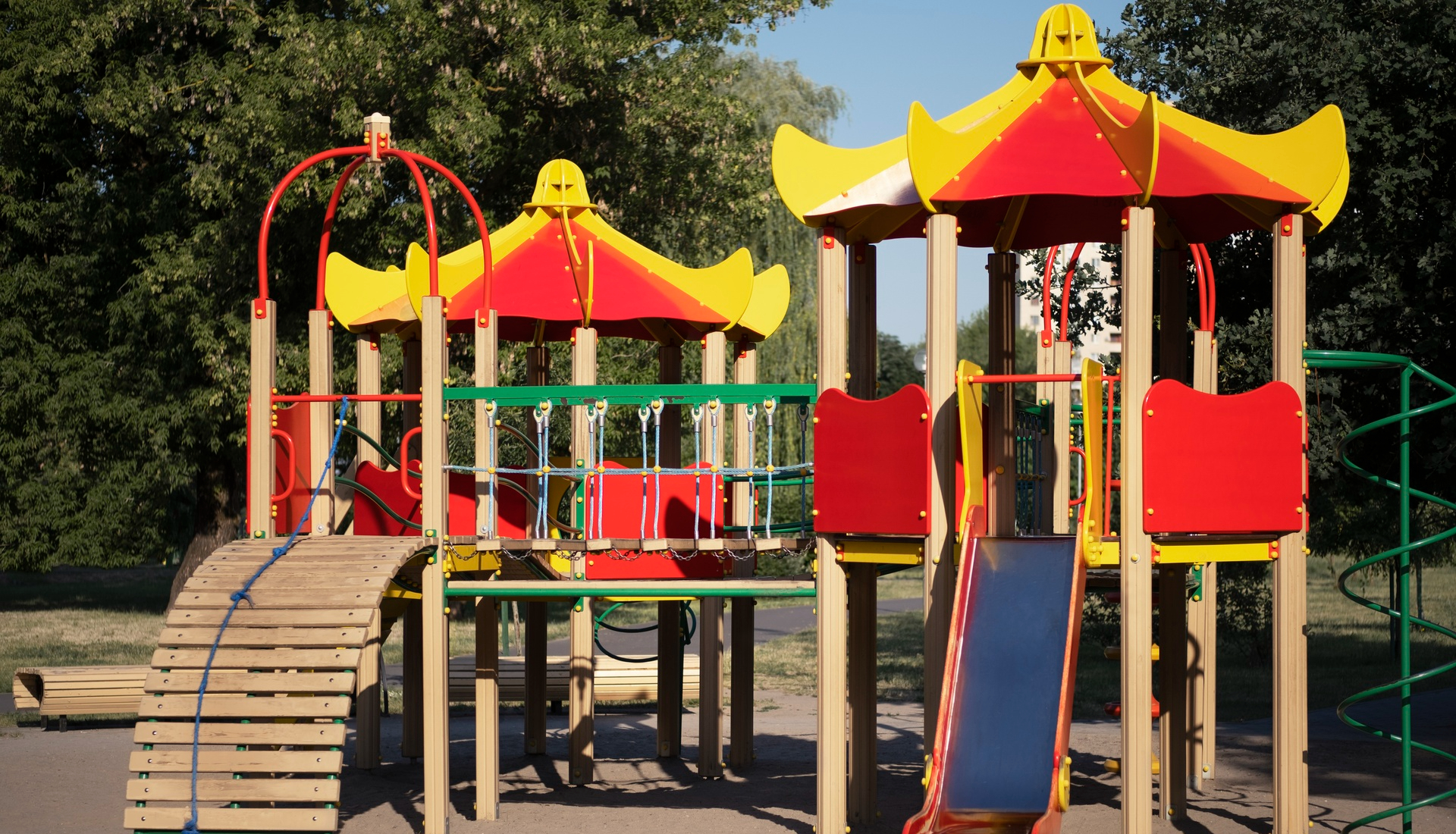 Zdjęcie przedstawia plac zabaw, na którym ustawiono domek z mostem, zjeżdżalnią i schodami z desek. 